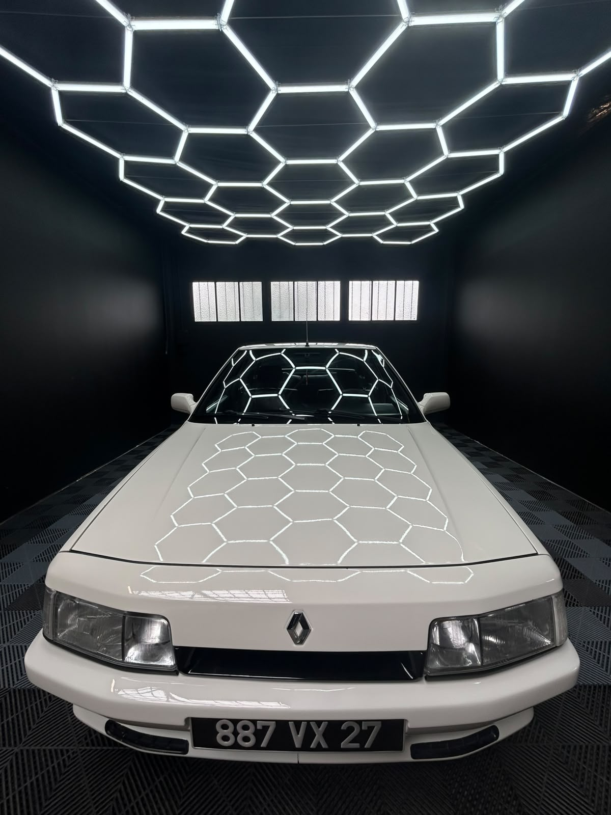 Renault 21 blanche brillante sous les éclairages hexagonaux de l'atelier