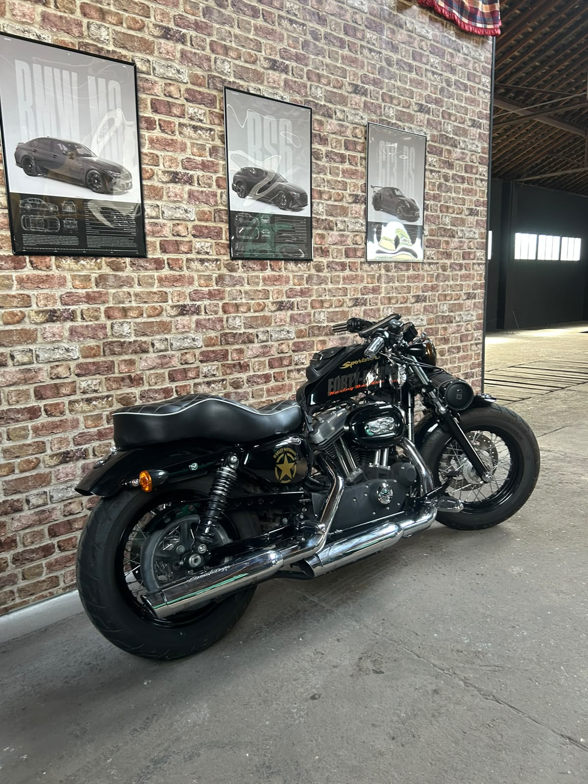 Moto Harley-Davidson noire préparée devant le mur de briques de l'atelier