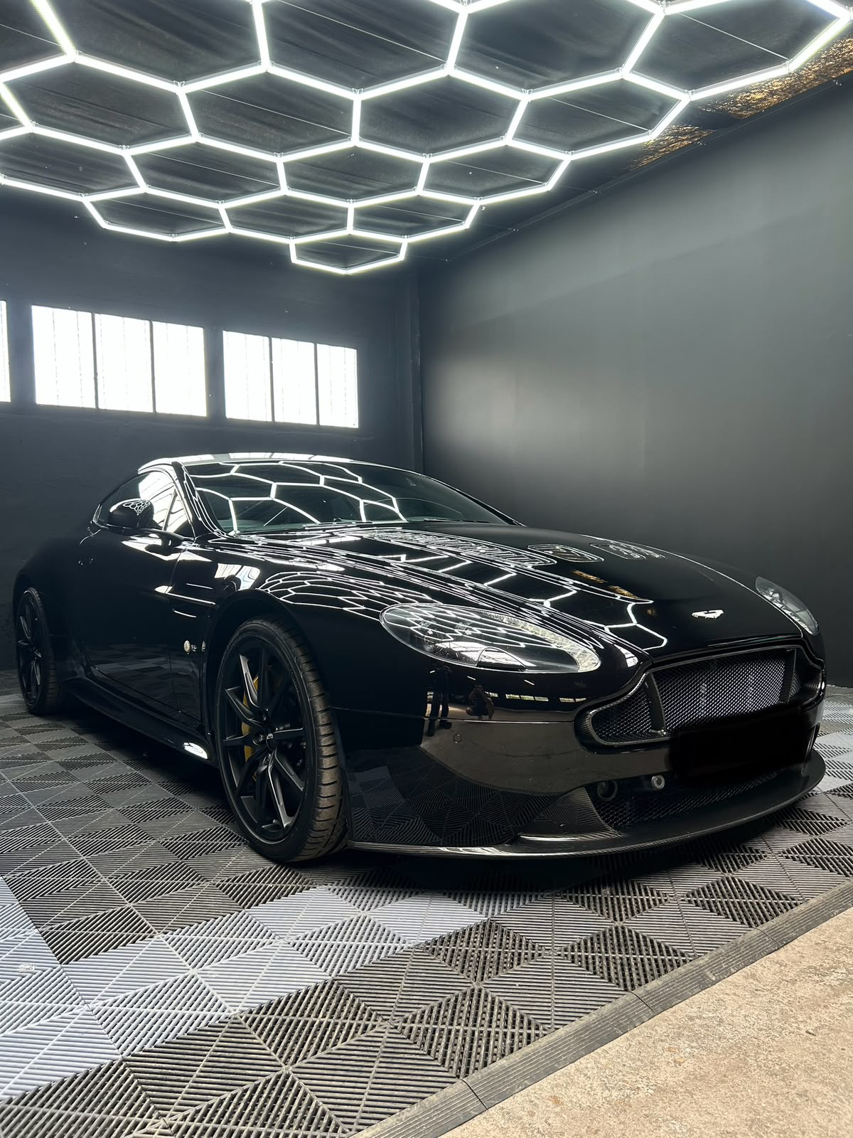 Aston Martin noire brillante sous les éclairages hexagonaux de l'atelier